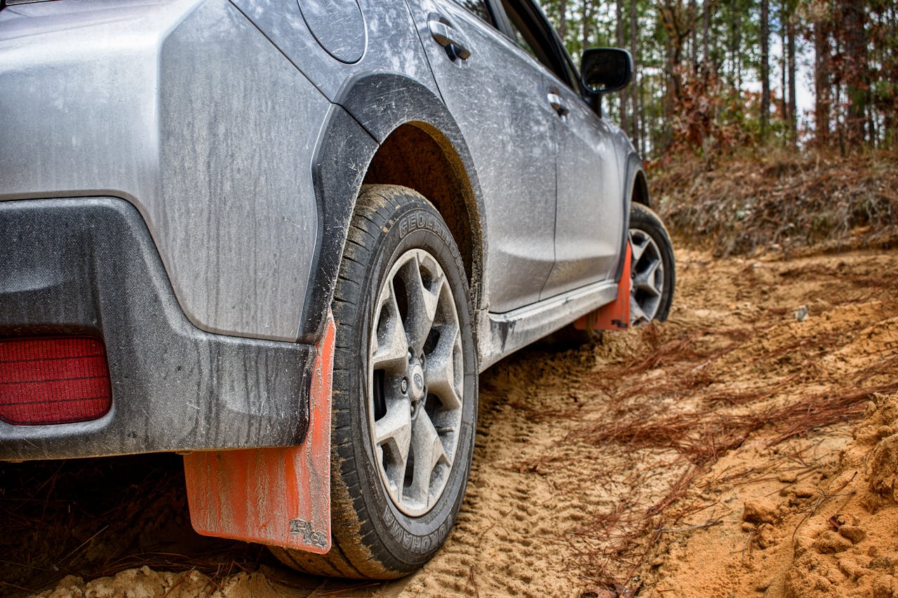 Close-up of a vehicle navigating muddy off-road terrain surrounded by trees.